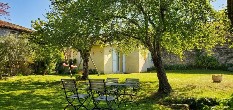 Table et chaises de jardin sous un arbre, pelouse et maison au fond