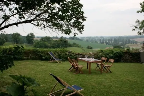 Transats et table sur la pelouse, campagne vallonnée à l’horizon