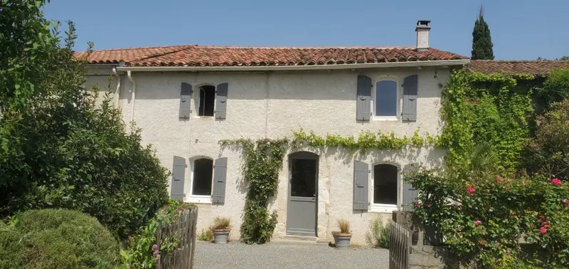 Façade en pierre de la maison principale, volets gris et vigne vierge