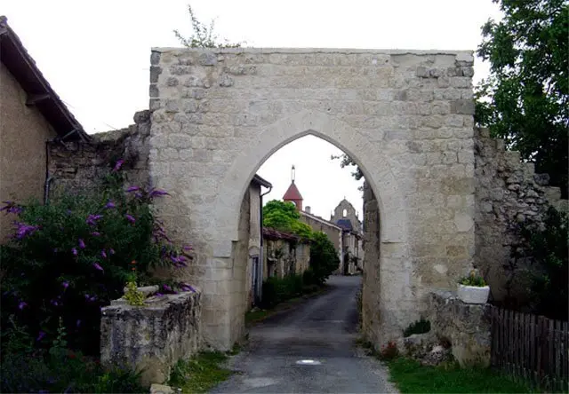 Porte fortifiée en pierre ouvrant sur la rue du village